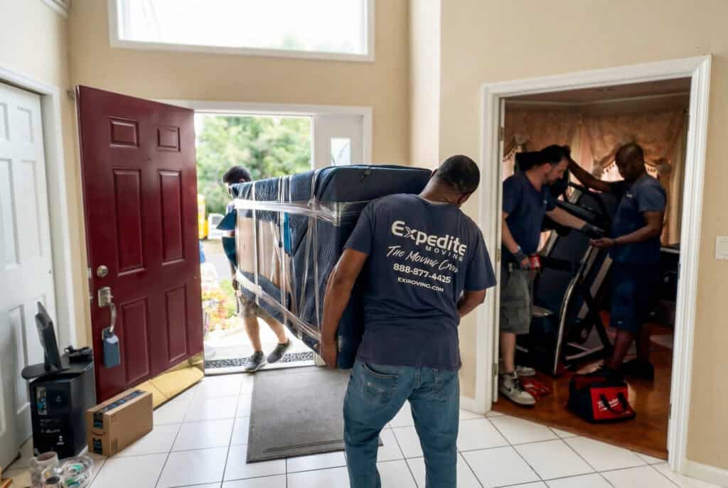 Movers carrying furniture out the front door towards the truck