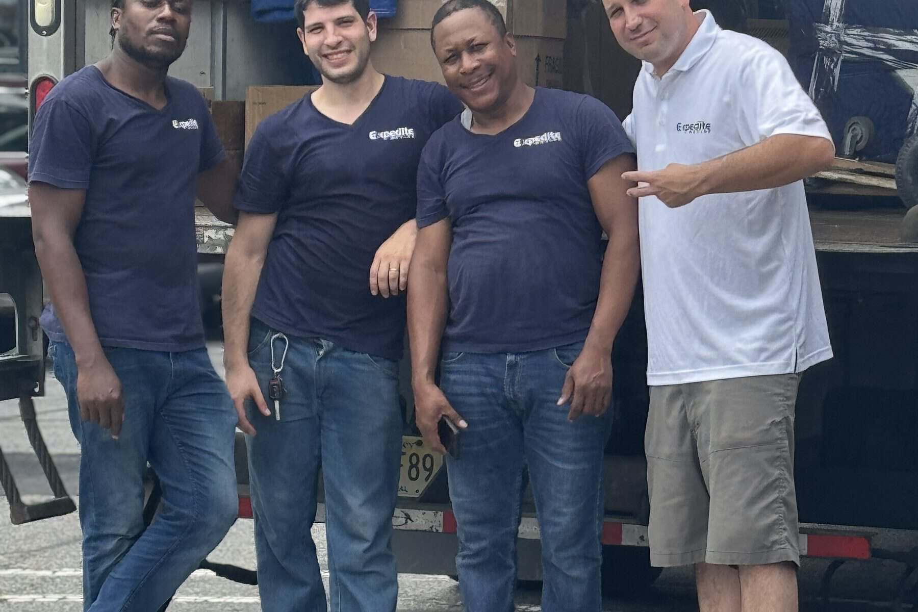 The Expedite Moving crew in branded shirts standing at the ramp of a loaded moving truck