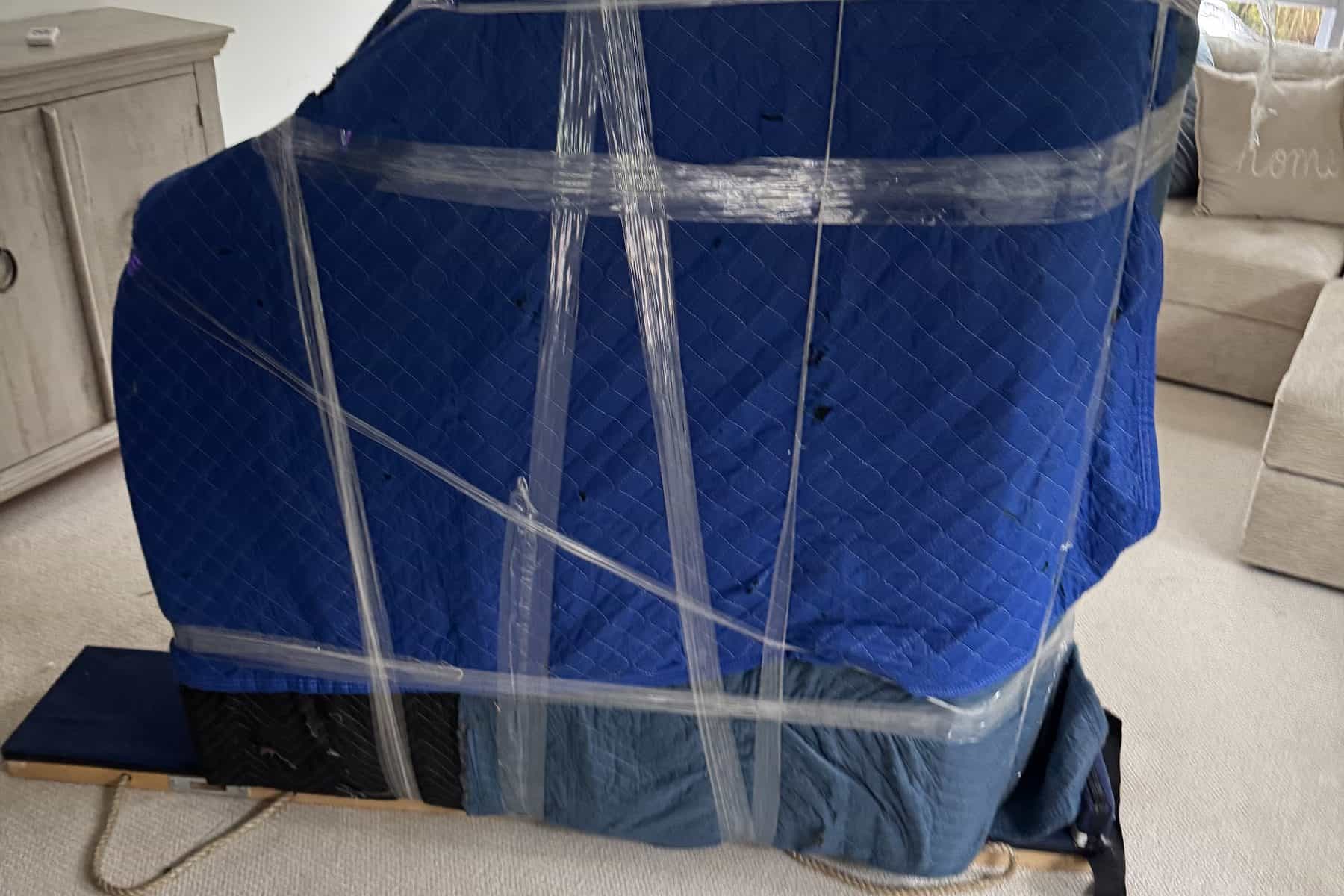 A tall piece of furniture wrapped in moving blankets and strapped to a four-wheel dolly in a Union County home