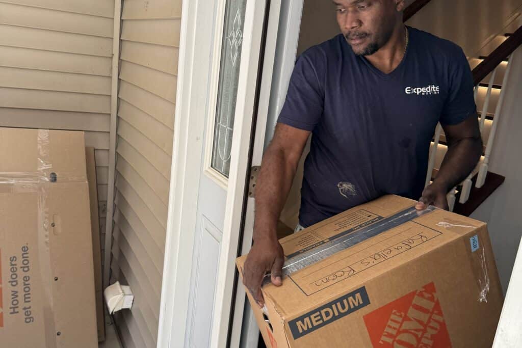 Expedite Moving crew member carrying a box through a front doorway