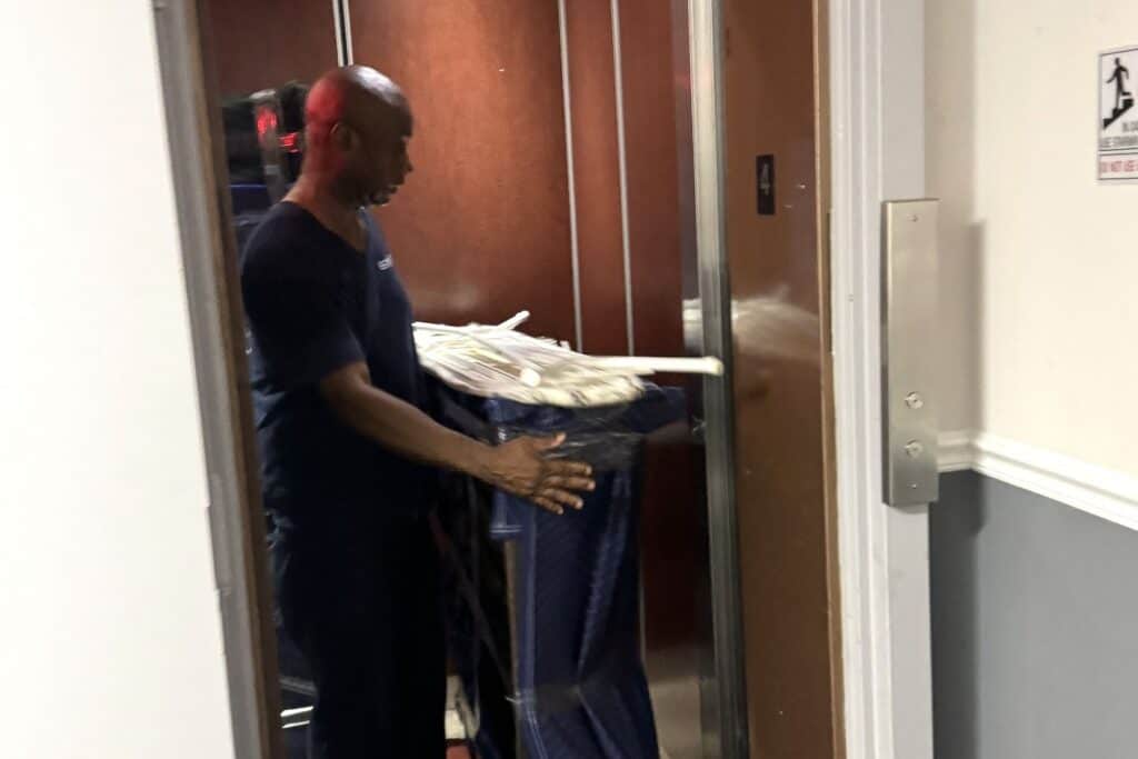 An Expedite Moving crew member guiding a blanket-wrapped load into an apartment building freight elevator