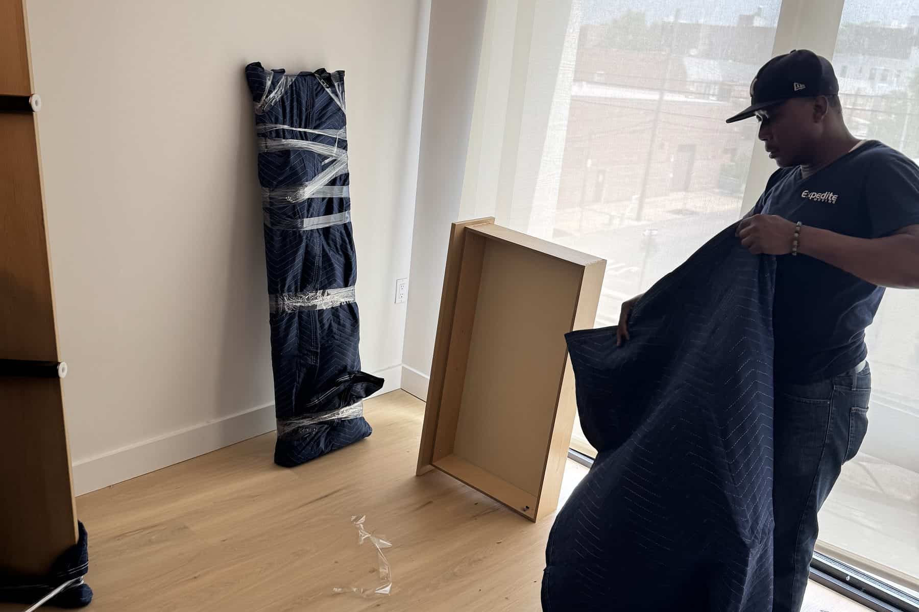 An Expedite Moving crew member laying a quilted moving blanket over a large framed piece, with another item already wrapped and taped behind