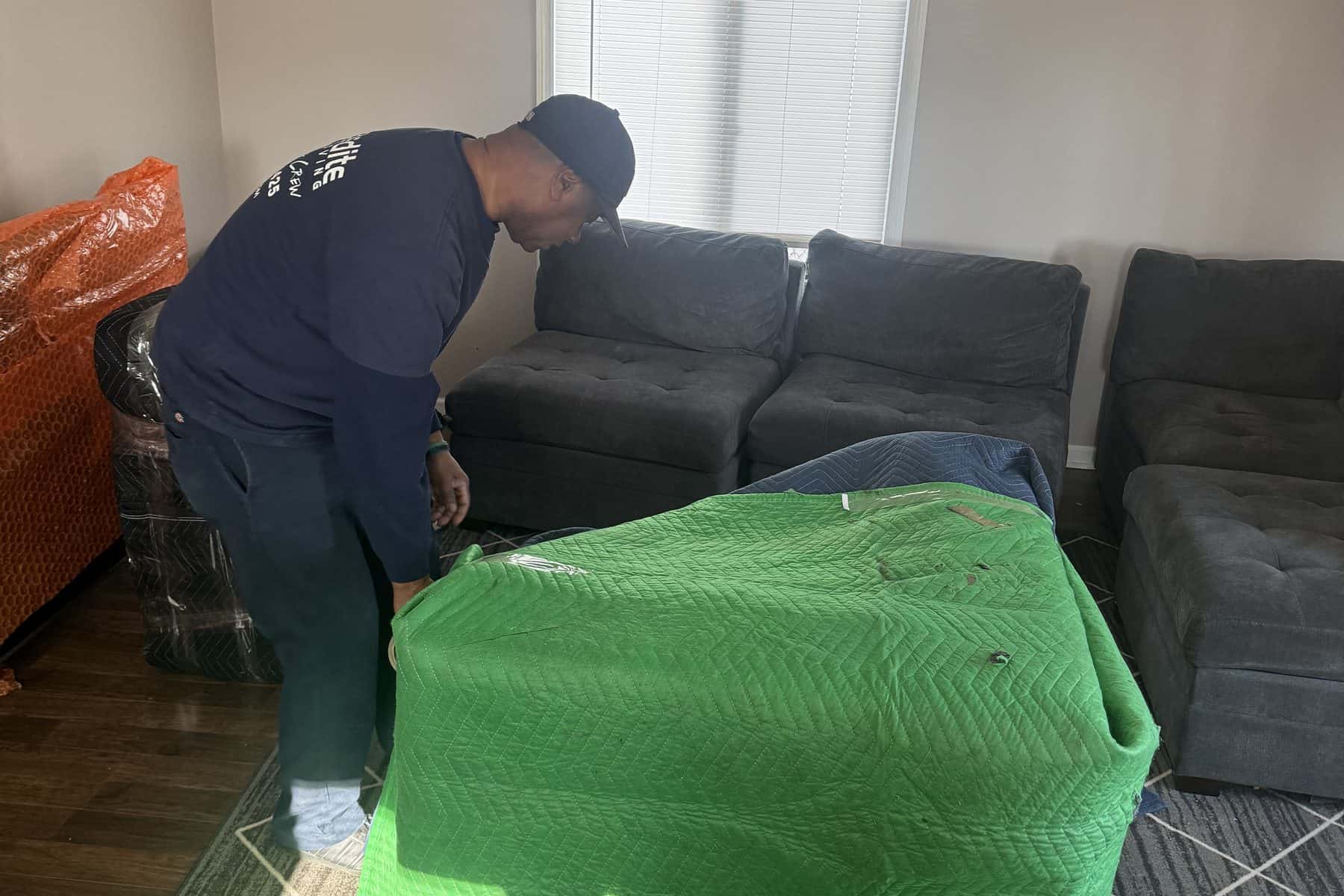 An Expedite Moving crew member wrapping a sectional sofa in protective moving blankets and stretch wrap